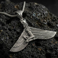 Load image into Gallery viewer, Oxidized winged goddess ankh pendant necklace on textured volcanic rock, centered close-up highlighting the spread wings, ankh bale detail, and deep antique shadowed contrast.
