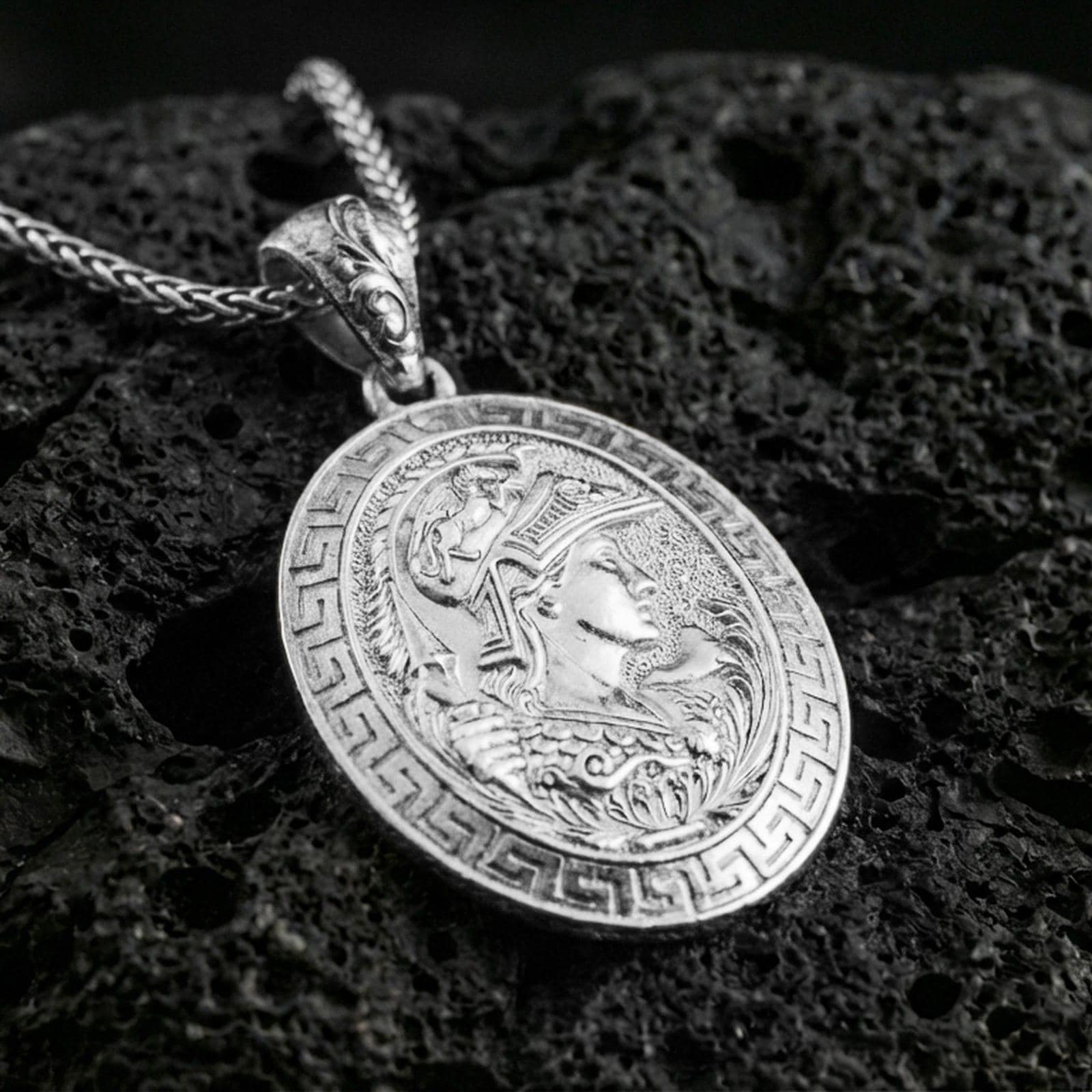 Polished silver Athena coin pendant necklace on textured volcanic rock, crisp macro product photo emphasizing clean edges, sharp engraving, and bright reflective highlights on the relief.