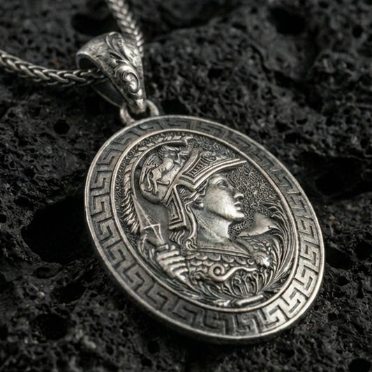 Oxidized Athena coin pendant necklace on textured volcanic rock, centered close-up highlighting the Greek key border, helmeted goddess profile, and deep antique shadowed contrast.