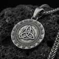 Load image into Gallery viewer, Oxidized celtic triquetra medallion pendant necklace on textured volcanic rock, centered close-up highlighting the Viking warrior relief detail, and deep antique shadowed contrast.

