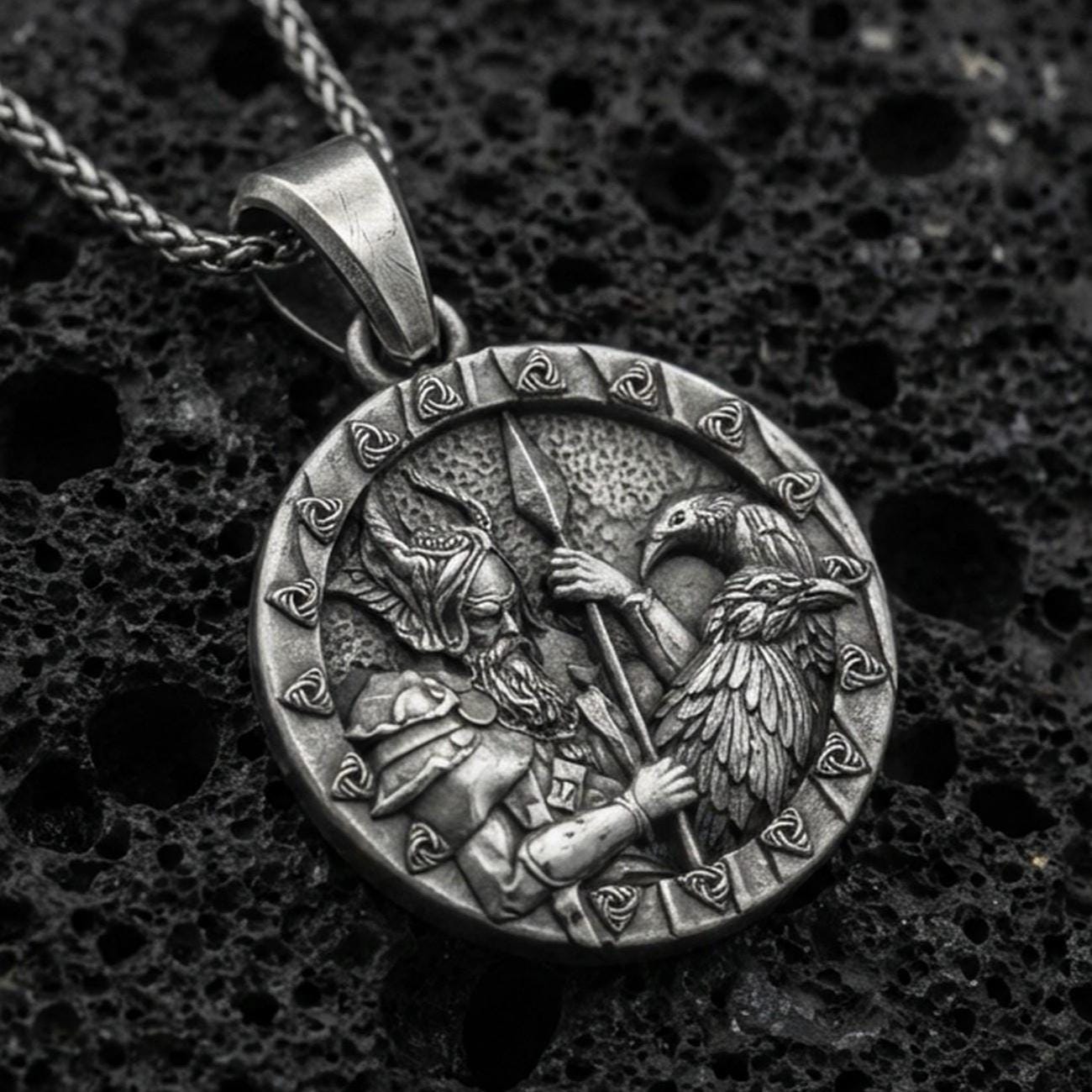 Oxidized Odin and raven medallion pendant necklace on textured volcanic rock, centered close-up highlighting the Viking warrior relief, spear detail, and deep antique shadowed contrast.