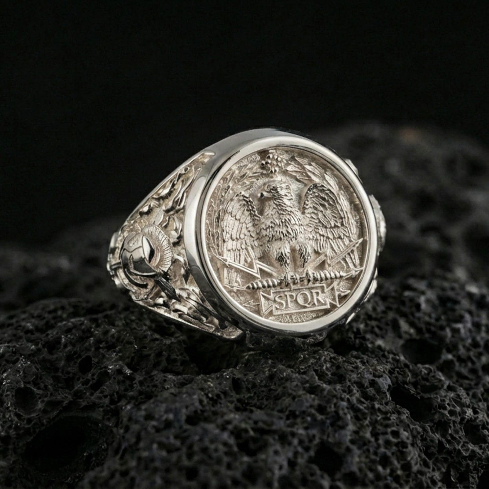 Polished silver SPQR coin style ring on textured volcanic stone, macro focus on the roman eagle emblem