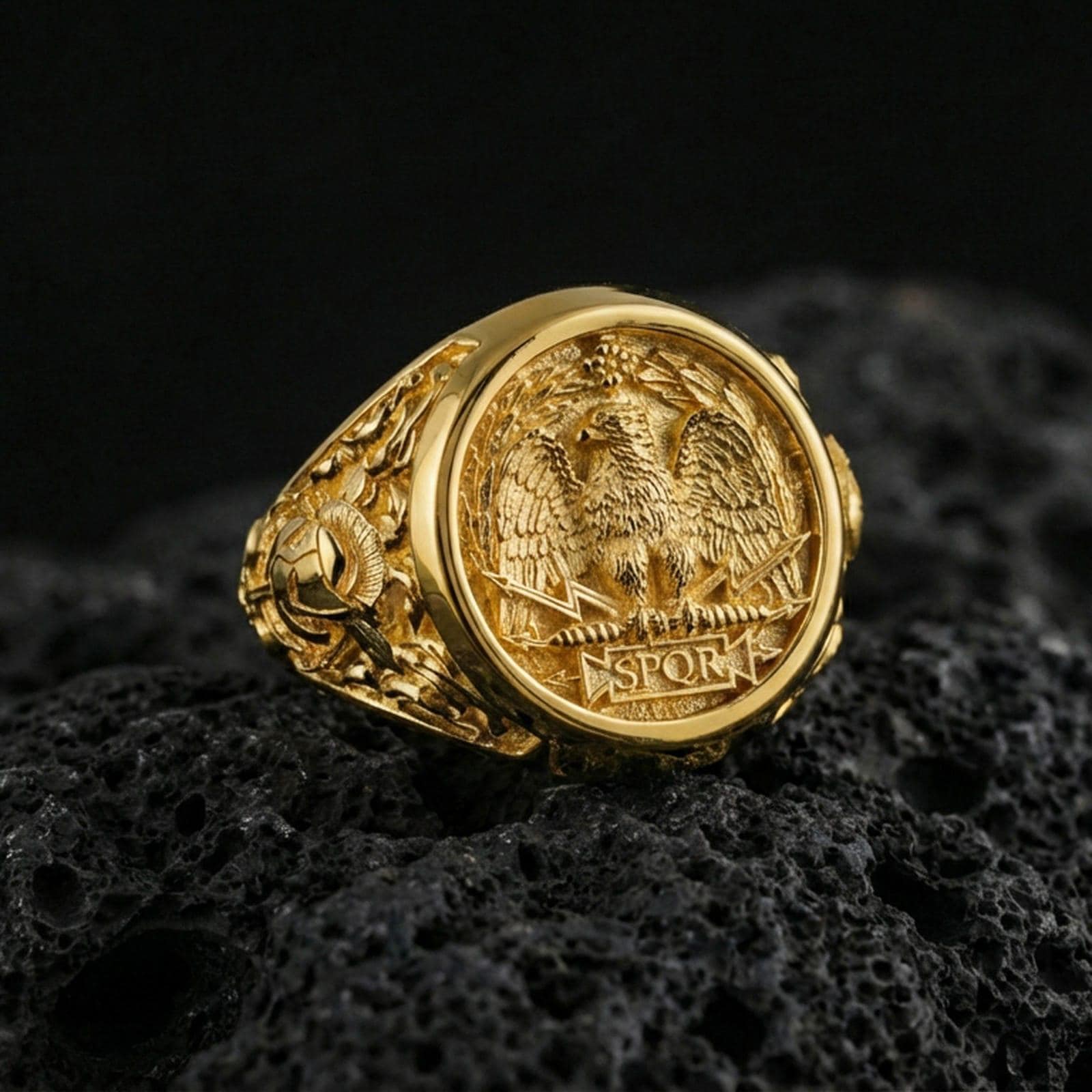 Gold plated SPQR signet ring on black volcanic rock with crisp highlights, showing the roman eagle and laurel details