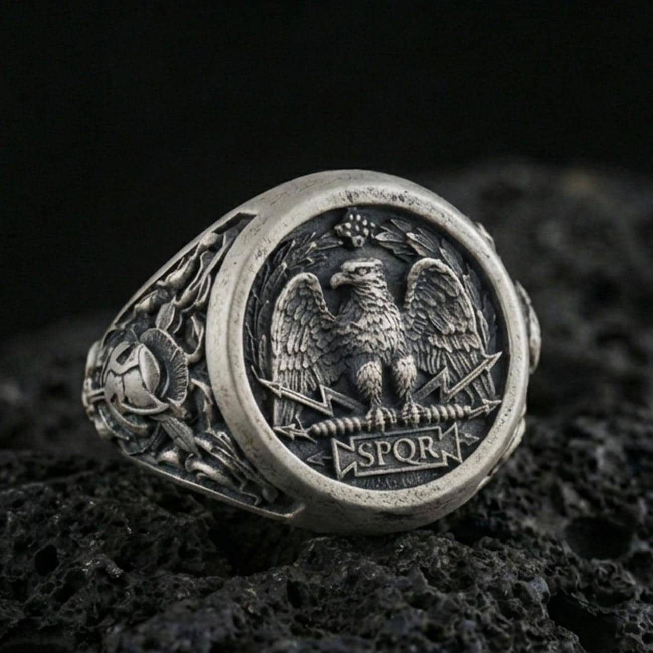 Close-up of an oxidized sterling silver SPQR roman eagle signet ring on porous volcanic rock in a dark studio