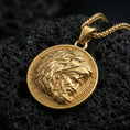 Load image into Gallery viewer, Gold plated Heracles lion helmet coin pendant necklace on textured volcanic rock, premium close-up with warm reflective shine across the lion head helmet, facial relief, and raised border pattern.
