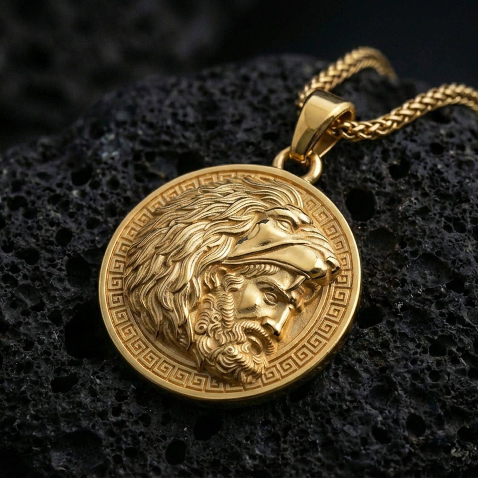 Gold plated Heracles lion helmet coin pendant necklace on textured volcanic rock, premium close-up with warm reflective shine across the lion head helmet, facial relief, and raised border pattern.