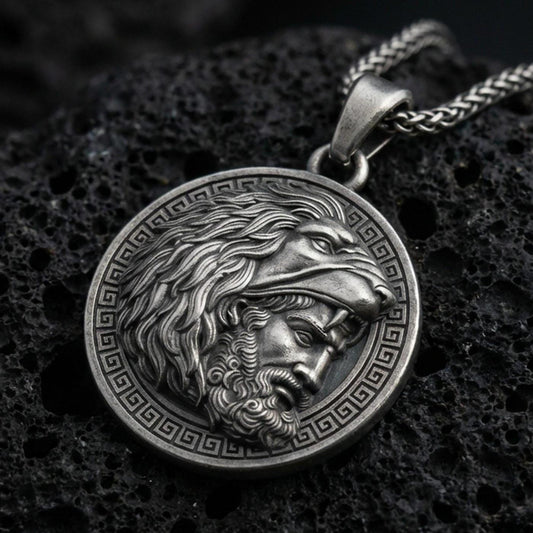Oxidized Heracles lion helmet coin pendant necklace on textured volcanic rock, centered close-up highlighting the Greek key border, lion head hood, and deep antique shadowed contrast.