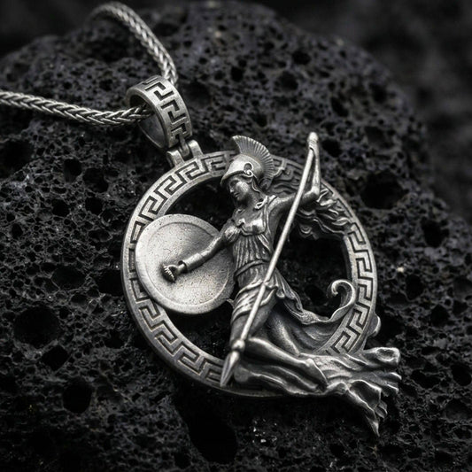 Oxidized Athena warrior pendant necklace on textured volcanic rock, centered close-up highlighting the Greek key frame, helmeted goddess figure, spear, and deep antique shadowed contrast.