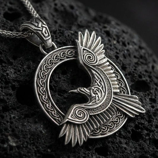 Oxidized Celtic raven knotwork pendant necklace on textured volcanic rock, centered close-up highlighting the winged raven silhouette, spiral accents, and deep antique contrast in the braided frame.