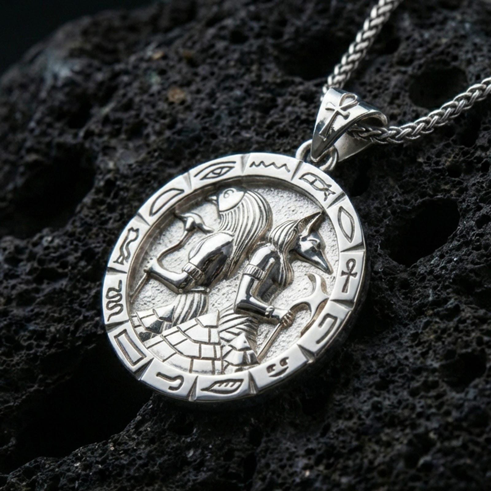 Polished silver Horus and Anubis pendant necklace on textured volcanic rock, crisp macro product photo emphasizing clean edges, sharp hieroglyph symbols, and bright reflective highlights on the relief.