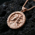 Load image into Gallery viewer, Rose gold plated Horus and Anubis pendant necklace on textured volcanic rock, centered studio-style close-up showcasing soft rosy glow and intricate Egyptian mythology engraving with clear hieroglyphic accents.
