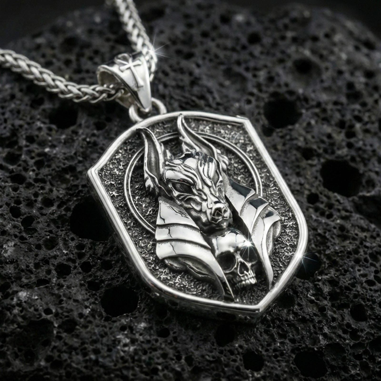 Polished silver Anubis pendant necklace on textured volcanic rock, crisp macro product photo emphasizing clean edges, sharp sculpted lines, and bright reflective highlights on the jackal mask relief.