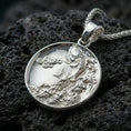 Load image into Gallery viewer, Polished silver koi fish medallion pendant necklace on textured volcanic rock, crisp macro product photo emphasizing clean edges, sharp scale engraving, and bright reflective highlights on the fish and waves.
