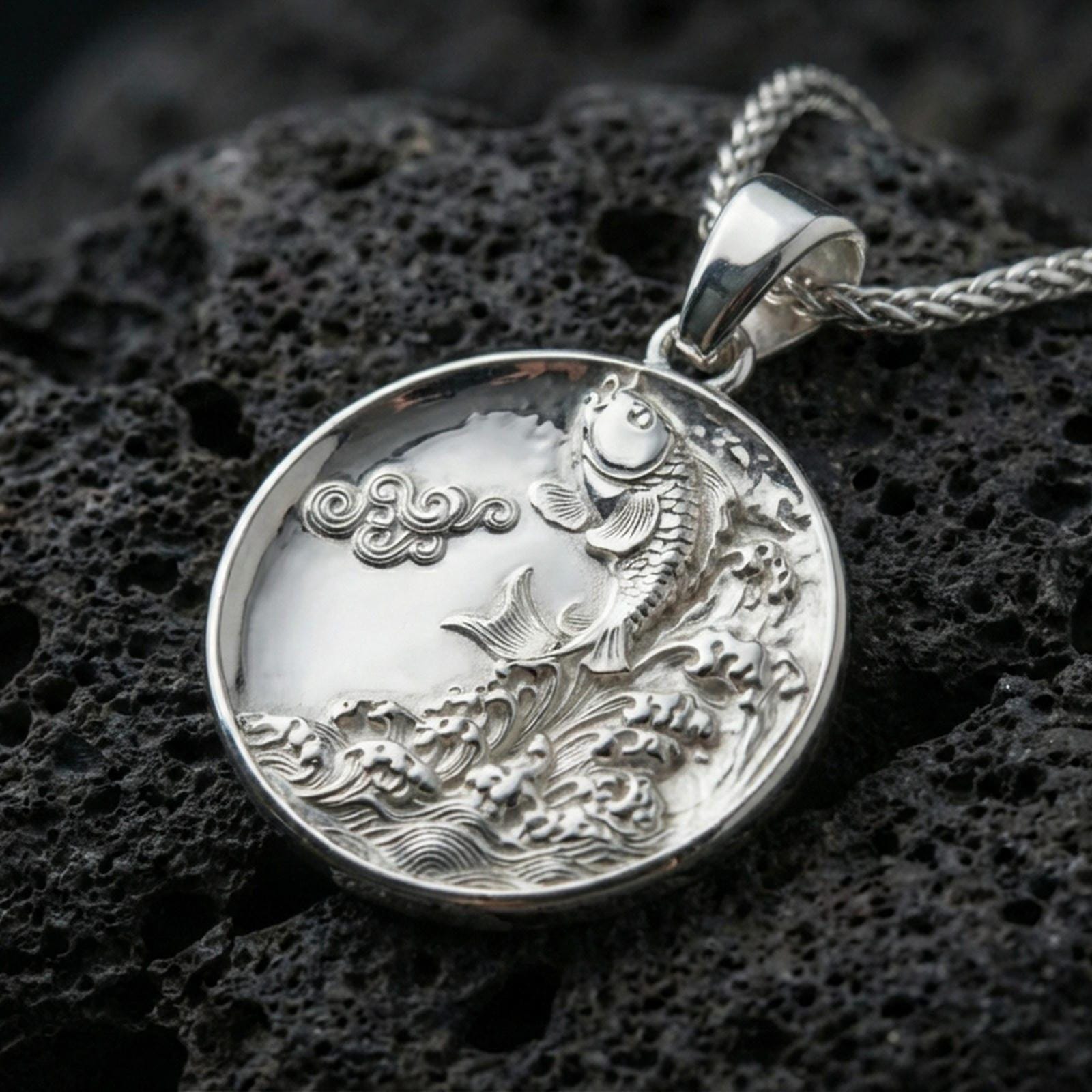 Polished silver koi fish medallion pendant necklace on textured volcanic rock, crisp macro product photo emphasizing clean edges, sharp scale engraving, and bright reflective highlights on the fish and waves.