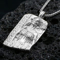Load image into Gallery viewer, Polished silver Hel Norse goddess pendant necklace on textured volcanic rock, crisp macro product photo emphasizing clean edges, sharp facial relief, and detailed textures on the hair, raven, and chain-like armor.

