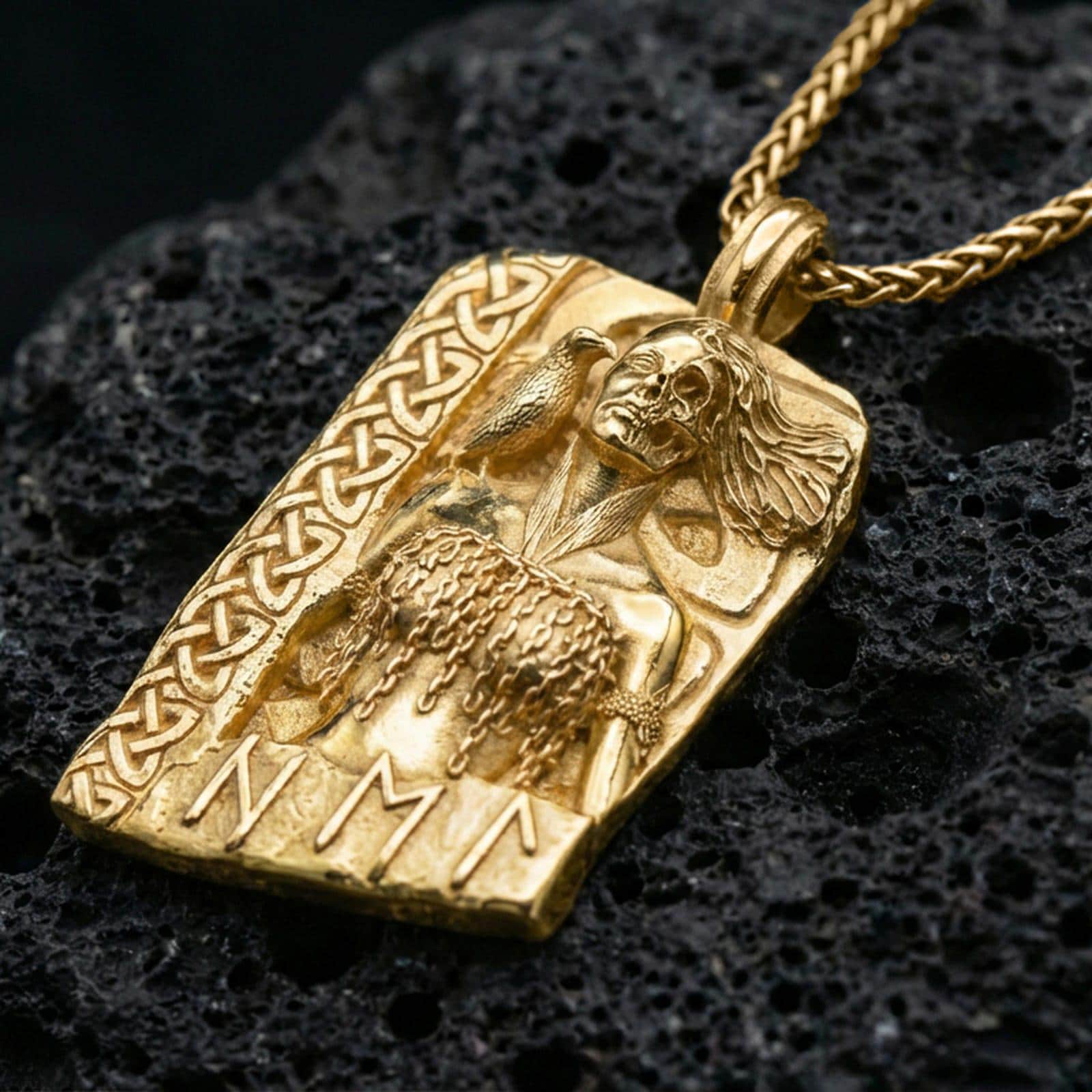 Gold plated Hel Norse goddess pendant necklace on textured volcanic rock, premium close-up with warm reflective shine across the half-skull portrait, braided border, and raised rune details.