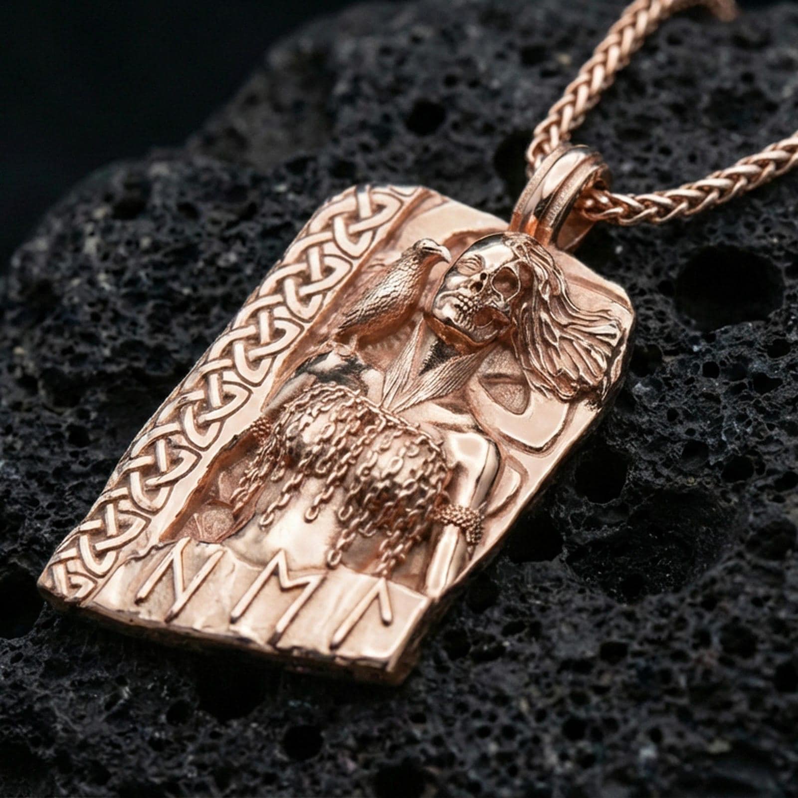 Rose gold plated Hel Norse goddess pendant necklace on textured volcanic rock, centered studio-style close-up showcasing soft rosy glow and intricate Norse relief detailing with clear rune accents.