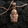 Load image into Gallery viewer, Rose gold plated Viking warrior head pendant necklace on textured volcanic rock, centered studio-style close-up showcasing soft rosy glow and intricate Norse helmet-and-beard detailing.
