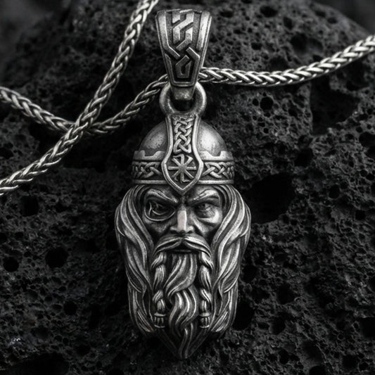 Oxidized Viking warrior head pendant necklace on textured volcanic rock, centered close-up highlighting the stern face, flowing beard, helmet rune detail, and deep antique shadowed contrast.