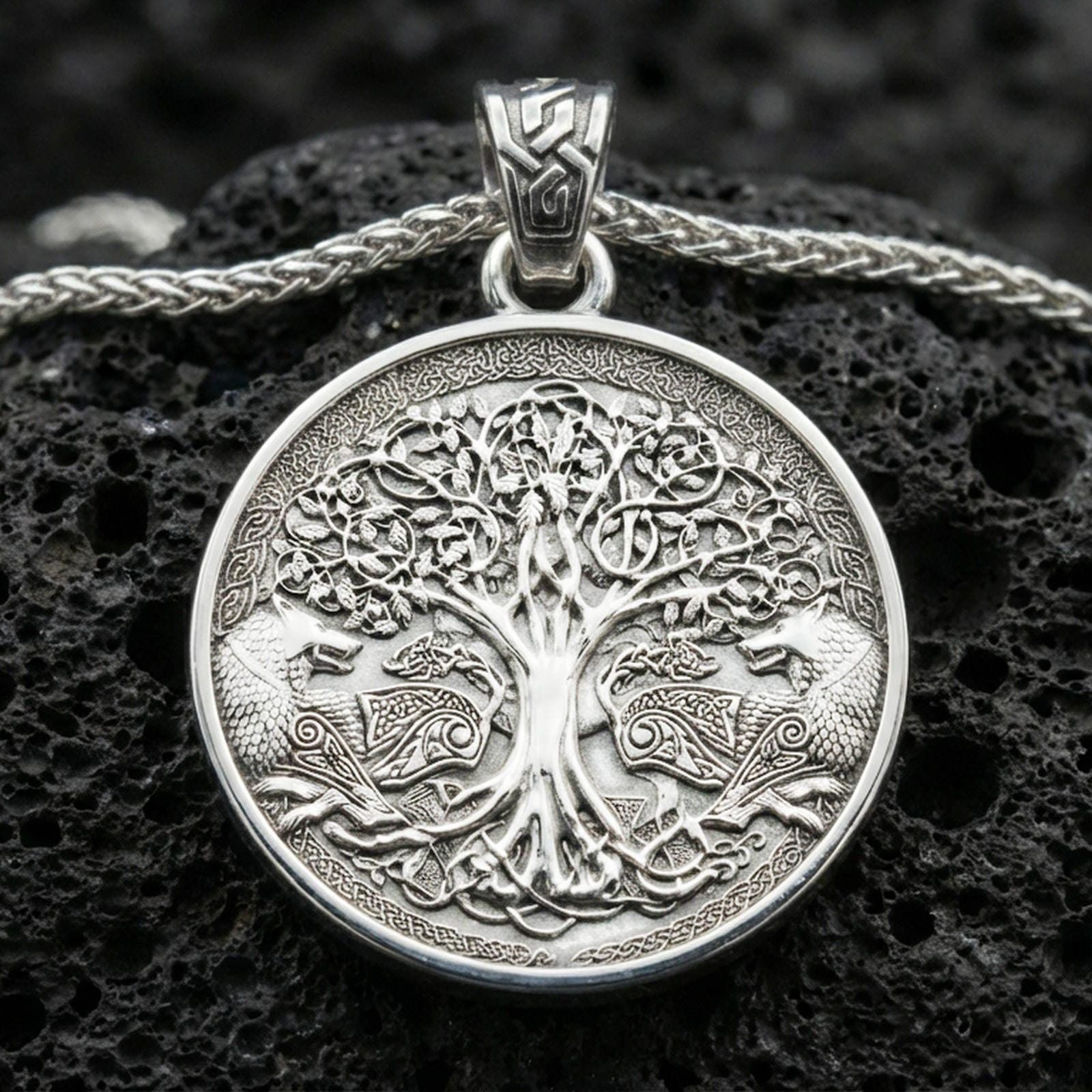 Polished silver Yggdrasil tree of life pendant necklace on textured volcanic rock, crisp macro product photo emphasizing clean edges, sharp knotwork engraving, and bright reflective highlights on the tree relief.
