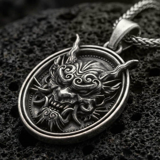 Oxidized demon mask medallion pendant necklace on textured volcanic rock, centered close-up highlighting the horned oni-style face, sharp fangs, and deep antique shadowed contrast.