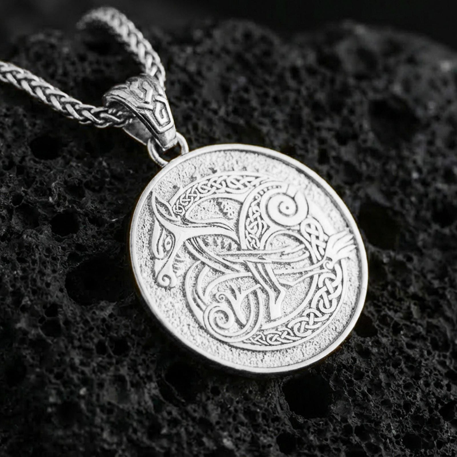Polished silver Urnes style Viking beast pendant necklace on textured volcanic rock, crisp macro product photo emphasizing clean edges, sharp scrollwork lines, and bright reflective highlights on the engraved design.