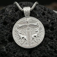 Load image into Gallery viewer, Polished silver Viking deer medallion pendant necklace on textured volcanic rock, crisp macro product photo emphasizing clean edges, sharp scroll engraving, and bright reflective highlights on the stags and border.
