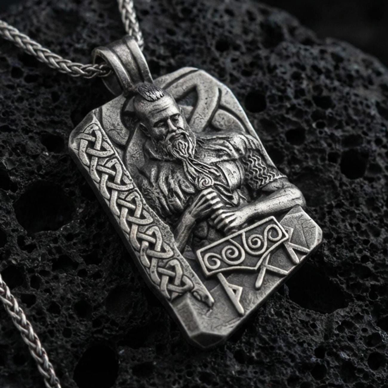 Oxidized Thor pendant necklace on textured volcanic rock, centered close-up highlighting the Norse god relief, Mjölnir hammer detail, rune lettering, and deep antique shadowed contrast.