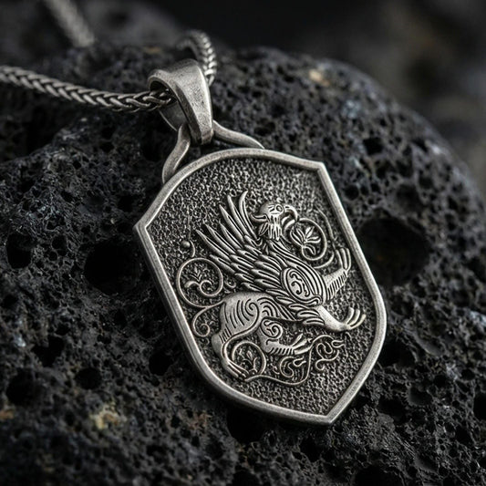 Oxidized griffin shield pendant necklace on textured volcanic rock, centered close-up highlighting the winged guardian gryphon, ornate scroll accents, and deep antique shadowed contrast.