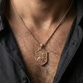 Load image into Gallery viewer, Rose gold plated griffin shield pendant necklace worn on the neck, lifestyle wear shot with elegant rosy shine and crisp wing-and-scroll detailing visible.
