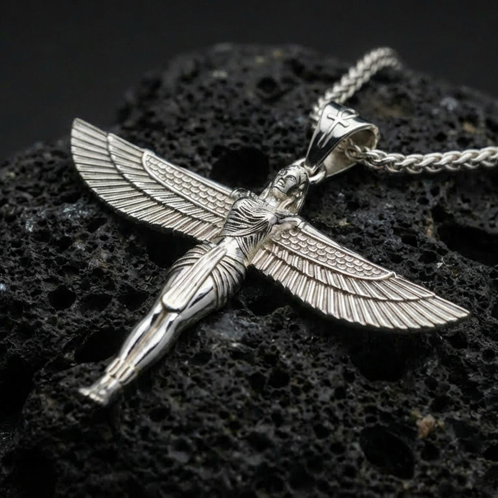 Polished silver winged Isis goddess pendant necklace on textured volcanic rock, crisp macro product photo emphasizing clean edges, sharp feather detailing, and bright reflective highlights on the figure.