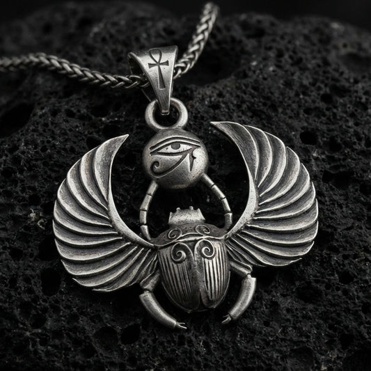 Oxidized winged scarab beetle pendant necklace on textured volcanic rock, centered close-up highlighting the spread wings, scarab body relief, Eye of Ra detail, and deep antique shadowed contrast.
