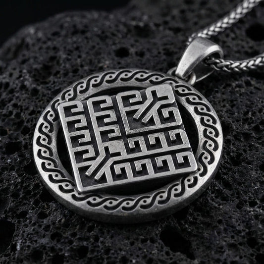 Oxidized geometric rune-style medallion pendant necklace on textured volcanic rock, centered close-up highlighting the raised maze-like symbol, patterned border, and deep antique shadowed contrast.