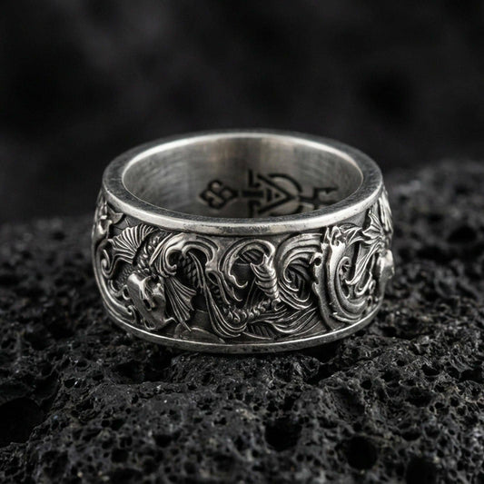 Oxidized koi fish band ring on textured volcanic rock, centered close-up highlighting the flowing koi relief, wave scrollwork, and deep antique shadowed contrast.