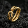 Load image into Gallery viewer, Gold plated snake wrap ring on textured volcanic rock, premium close-up with warm reflective shine across the coiled snake form and detailed scale pattern.
