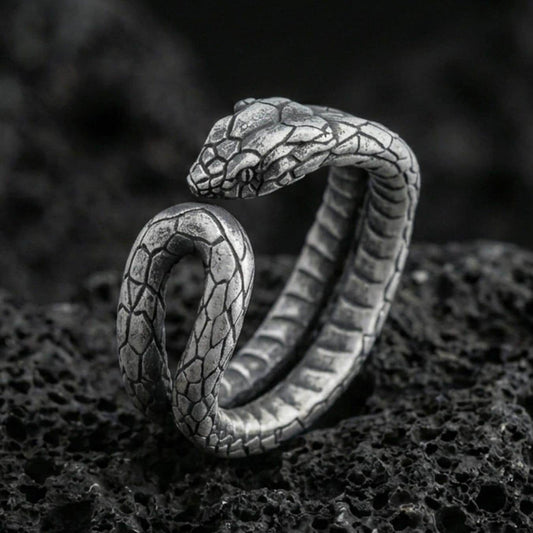 Oxidized snake wrap ring on textured volcanic rock, centered close-up highlighting the coiled body, scale texture, and deep antique shadowed contrast.