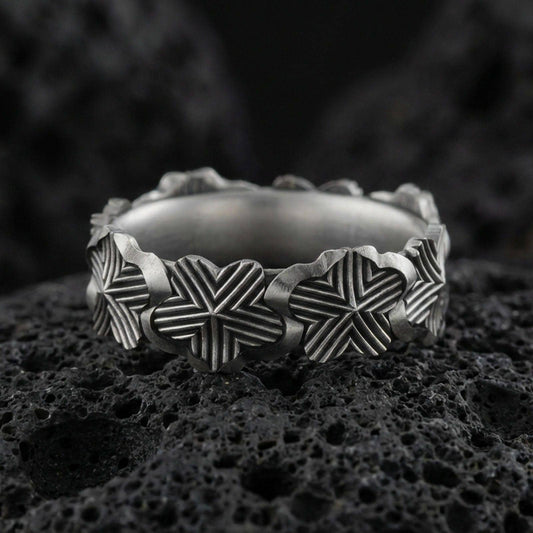 Oxidized floral band ring on textured volcanic rock, centered close-up highlighting the raised lily motifs, carved line texture, and deep antique shadowed contrast.