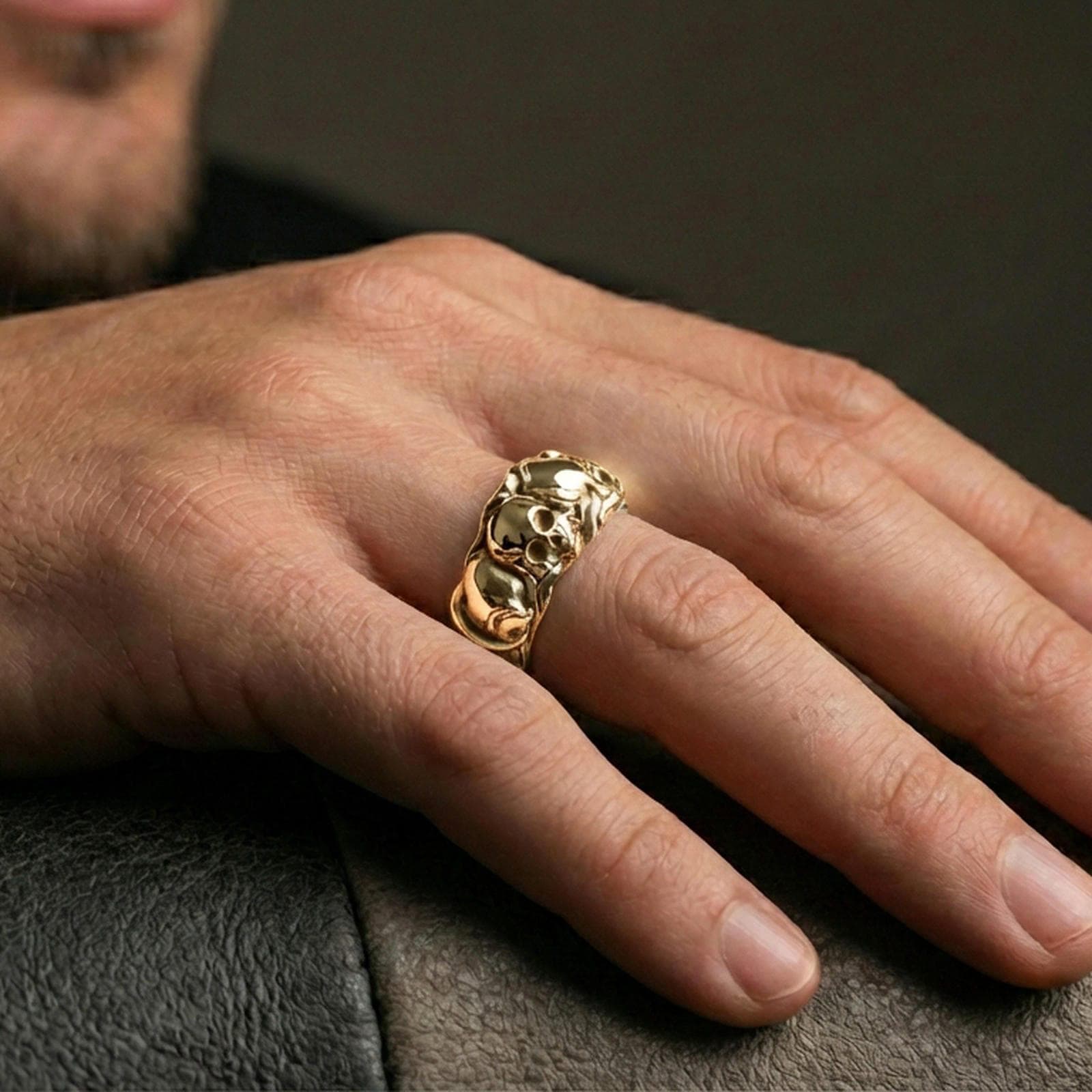 Gold plated skull band ring worn on a finger, lifestyle photo featuring warm tone finish and strong statement band presence.