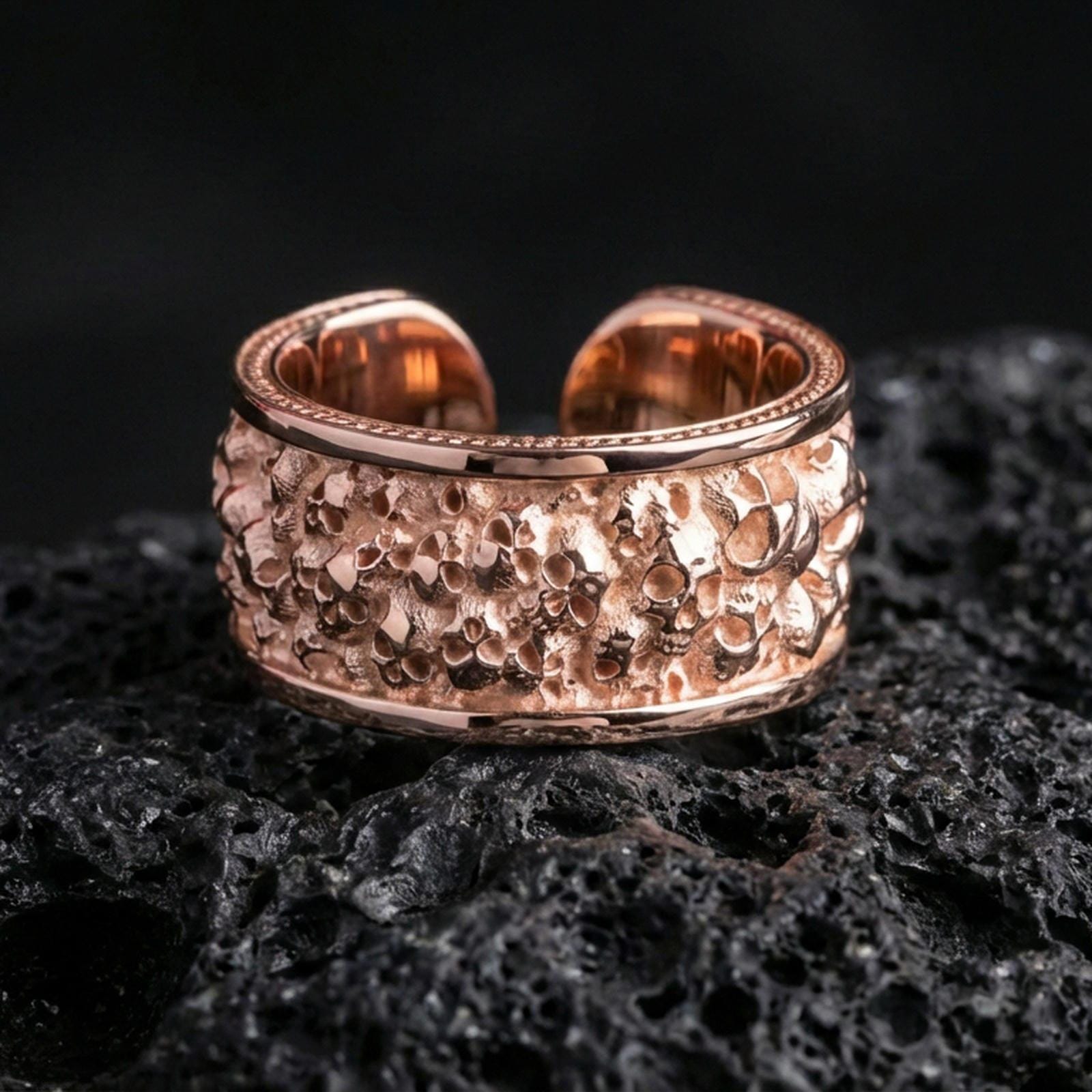 Rose gold plated skull cuff ring on textured volcanic rock, centered studio-style close-up showcasing soft rosy glow and crisp skull detailing with a refined finish.