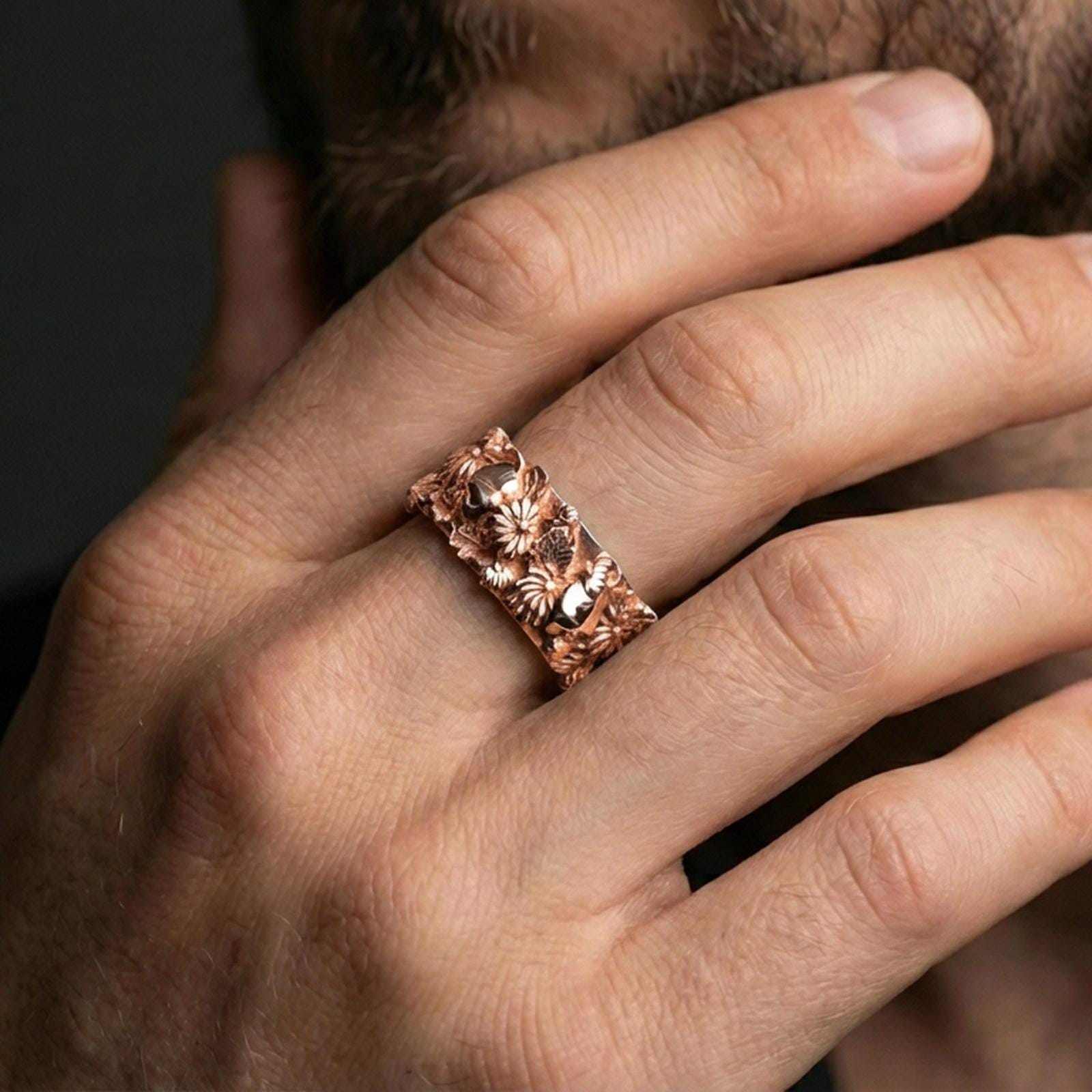 Rose gold plated skull and floral band ring worn on a finger, lifestyle wear shot with elegant rosy shine and crisp floral-and-skull detailing visible.