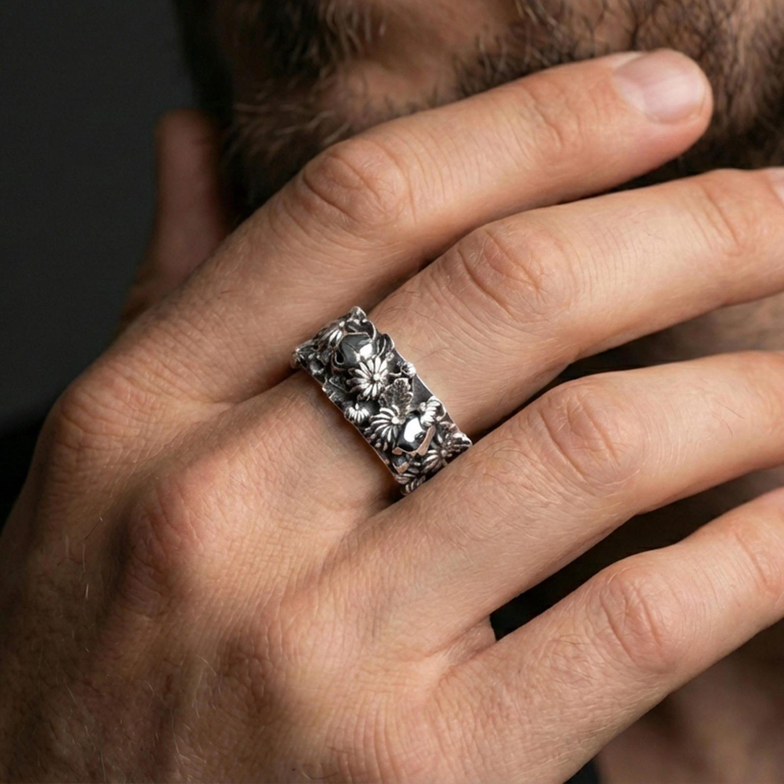 Polished silver skull and floral band ring worn on a finger, clean lifestyle wear shot capturing bright shine and the detailed skull-and-flower relief in natural light.