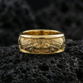 Load image into Gallery viewer, Gold plated twin lion band ring on textured volcanic rock, premium close-up with warm reflective shine across the lion profiles, raised contours, and detailed mane texture.
