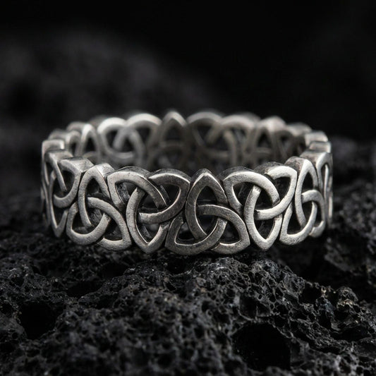 Oxidized Celtic triquetra chain-link ring on textured volcanic rock, centered close-up highlighting the interwoven Trinity knot links and deep antique shadowed contrast.