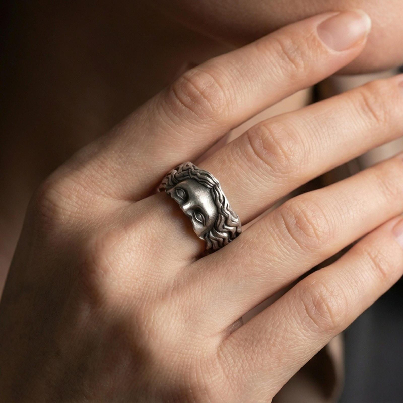 Oxidized face relief band ring worn on a finger, lifestyle framing showing realistic scale and bold vintage contrast in a natural hand pose.