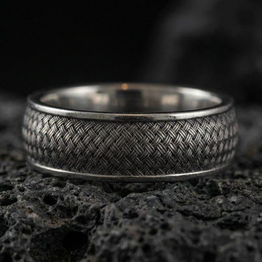 Oxidized woven texture band ring on textured volcanic rock, macro close-up highlighting the darkened braided pattern and antique silver contrast.