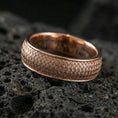 Load image into Gallery viewer, Rose gold plated woven texture band ring on textured volcanic rock, refined macro product shot capturing soft rosy highlights on the woven pattern and rounded band profile.
