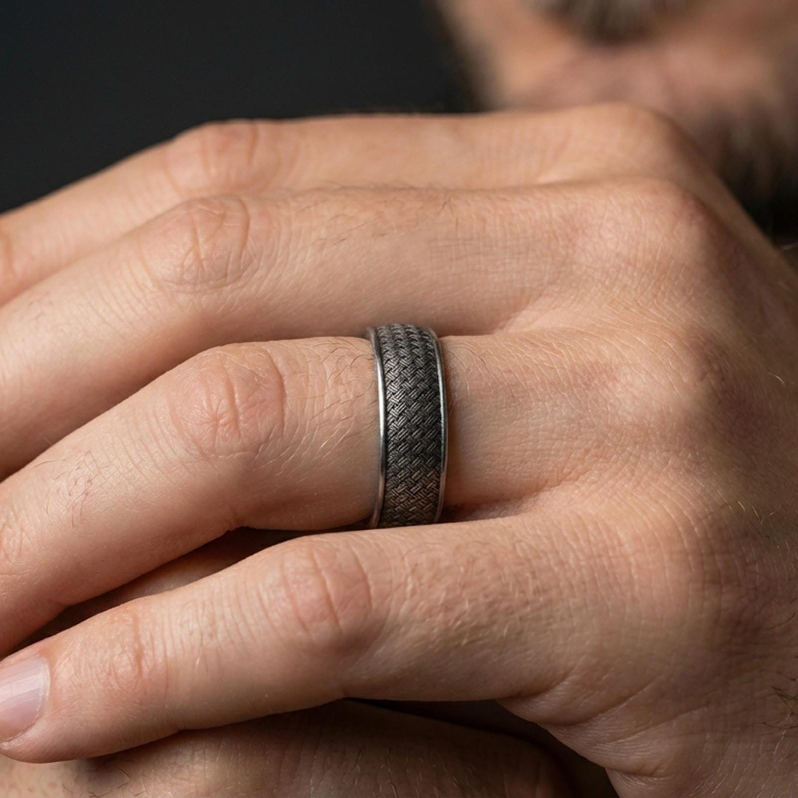 Oxidized woven texture band ring worn on a finger, lifestyle wear shot showing the darkened braid texture at real scale with natural hand posture.