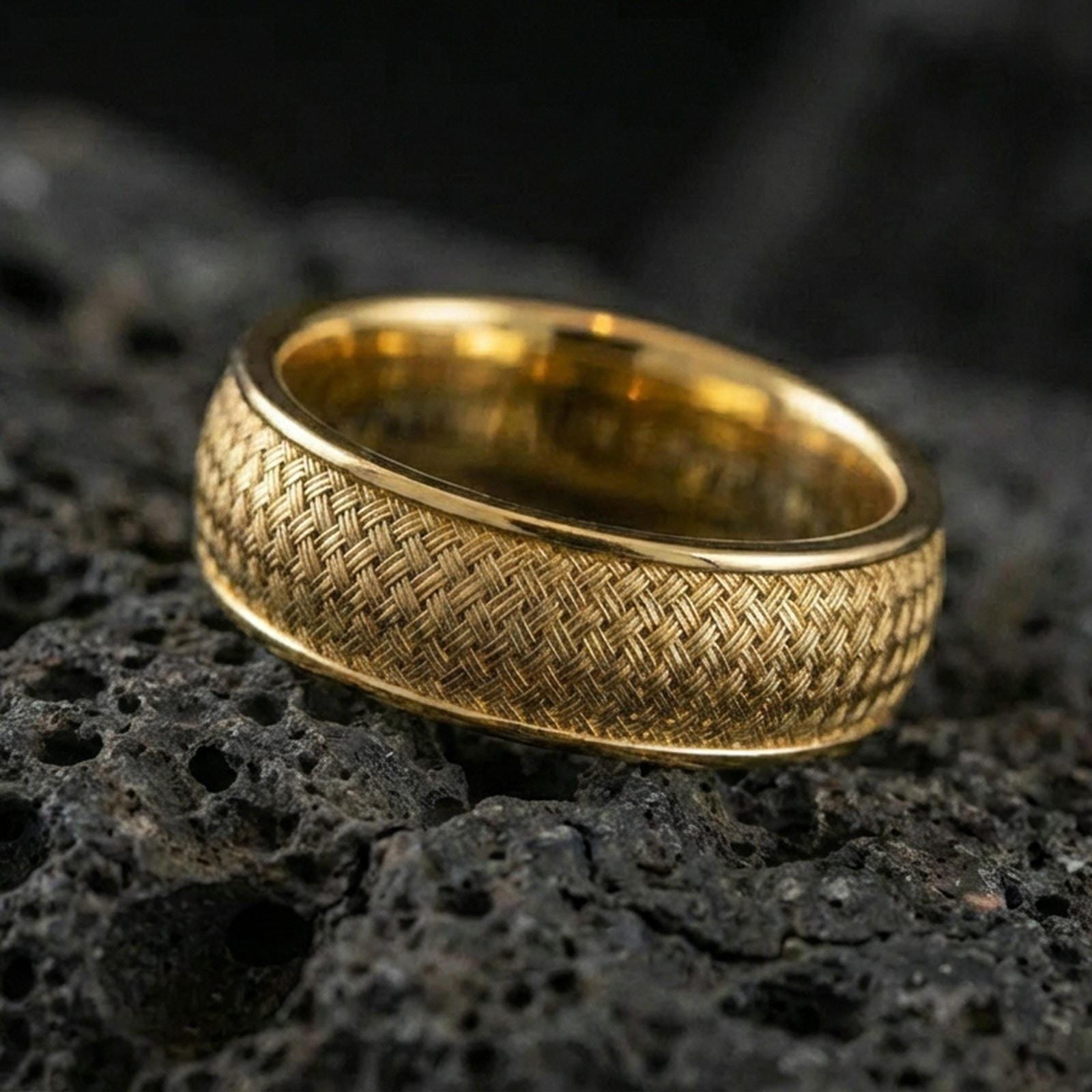 Gold plated woven texture band ring on textured volcanic rock, premium close-up showing warm gold tone across the braided surface and smooth edges.