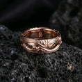 Load image into Gallery viewer, Rose gold plated scrollwork band ring on textured volcanic rock, refined macro product shot capturing soft rosy highlights and the dimensional scroll engraving.
