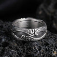 Load image into Gallery viewer, Oxidized scrollwork band ring on textured volcanic rock, macro close-up highlighting the darkened recessed background and raised flowing wave motifs.
